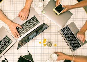 Top view of a team collaborating with laptops, phones, and notes in a modern office.